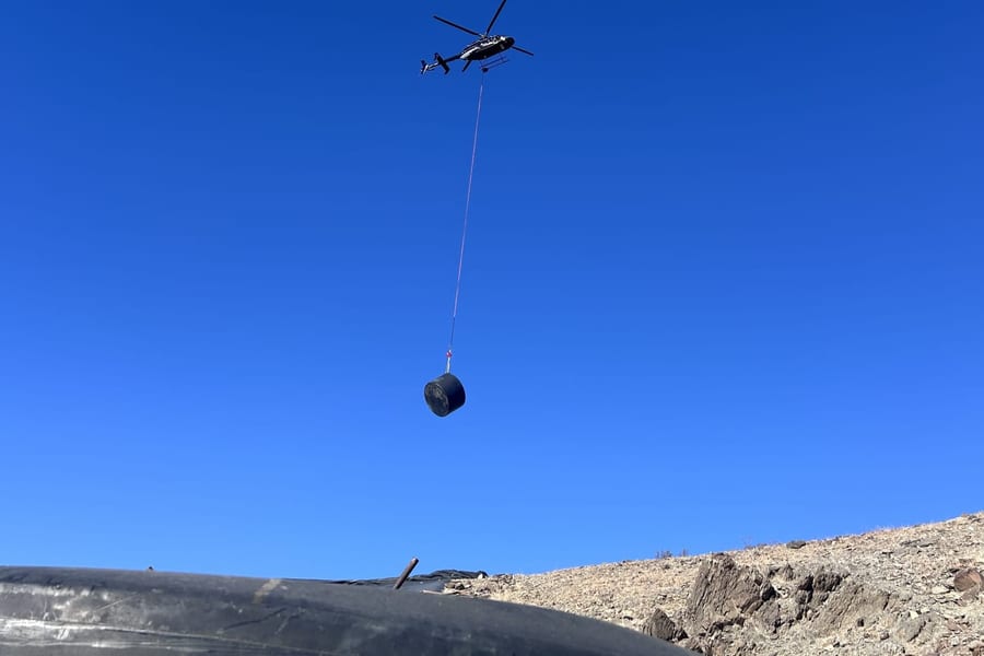 A helicopter long-lining a water tank above the Orocopia Mountains