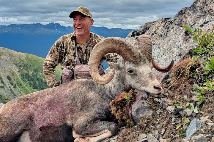 A smiling hunter behind a Stone’s ram on a rocky British Columbia ridge