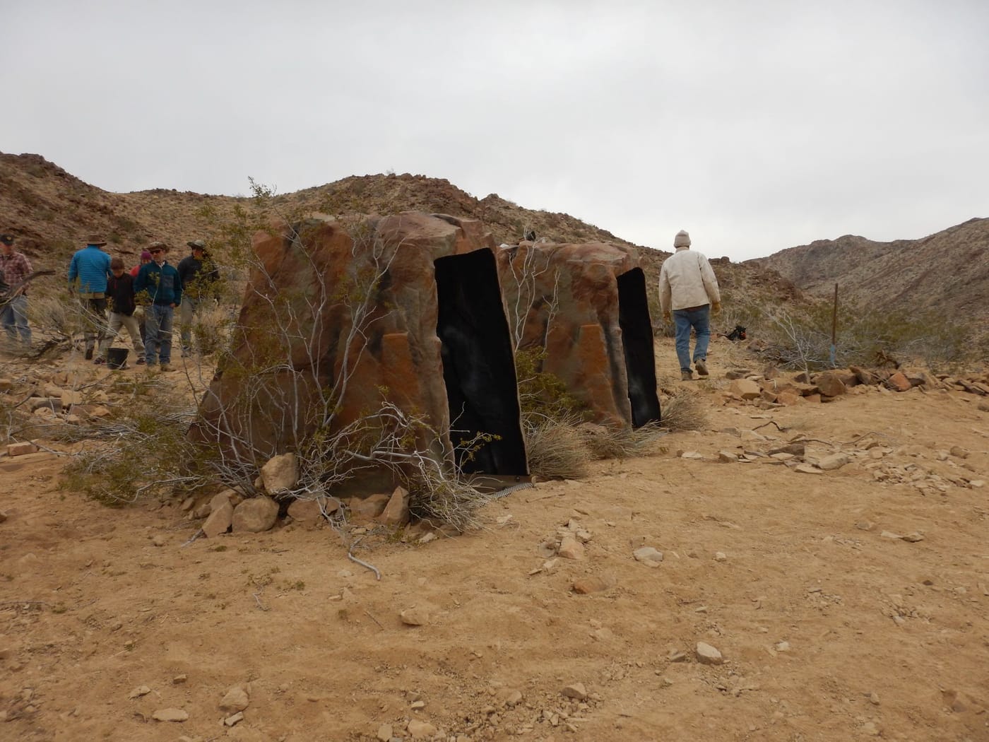 Two drinker housings shaped and colored like rock outcrops stand among desert scrub as volunteers walk by