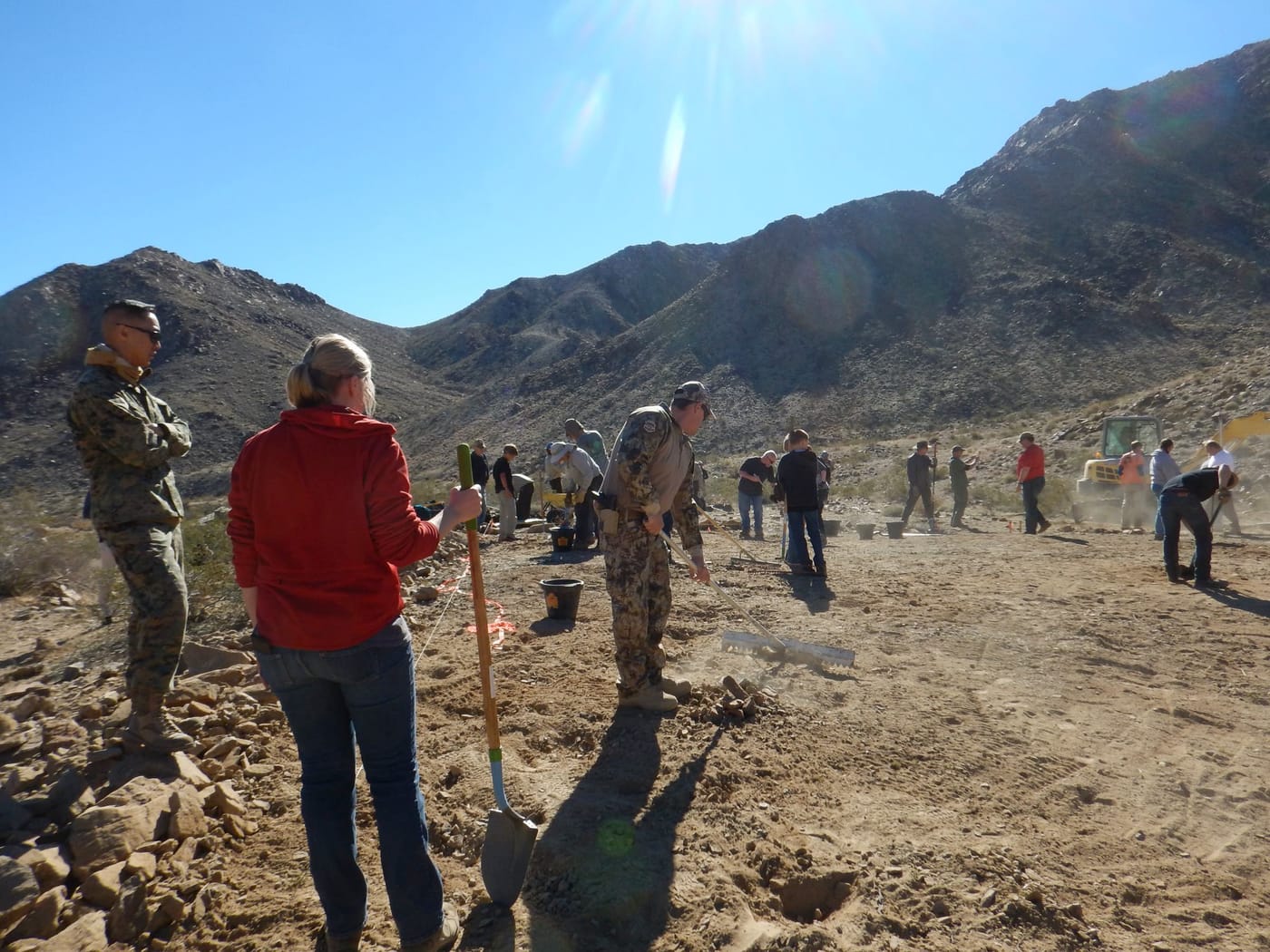 Volunteers with shovels and rakes level the cleared ground, two of them in camouflage uniforms
