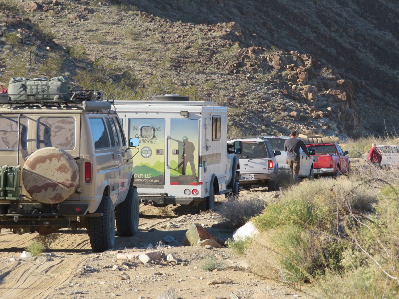 Four-wheel-drive vehicles, one a California Conservation Corps crew truck, lined up on a sandy desert track