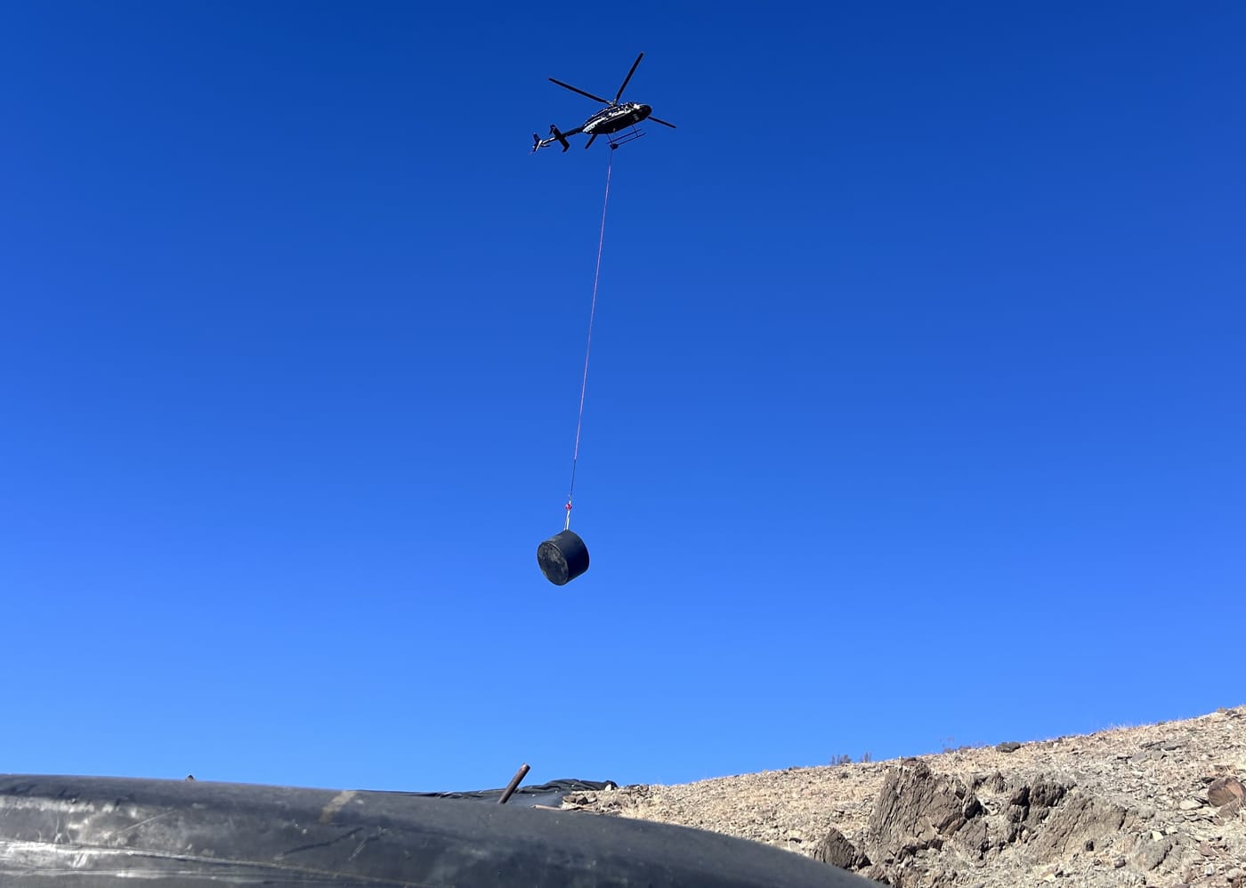 A helicopter carrying a water tank into the Orocopia Mountains