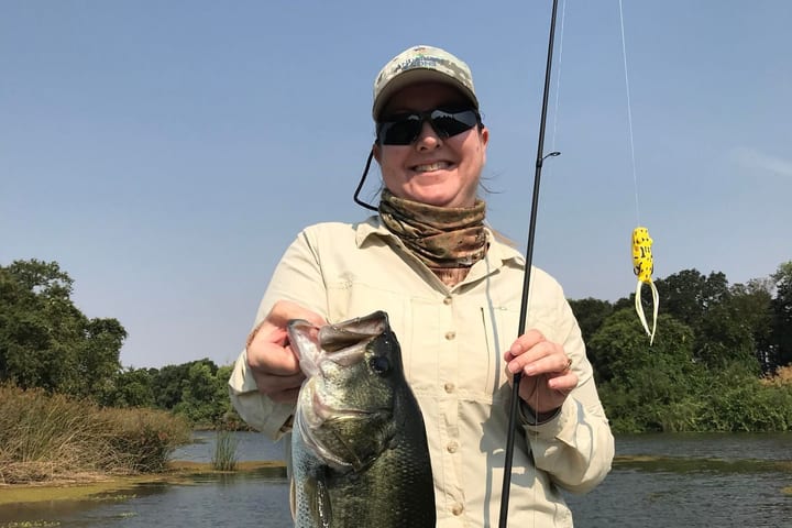 Katie Garrison-Martin on a boat, smiling behind a largemouth bass she has just landed